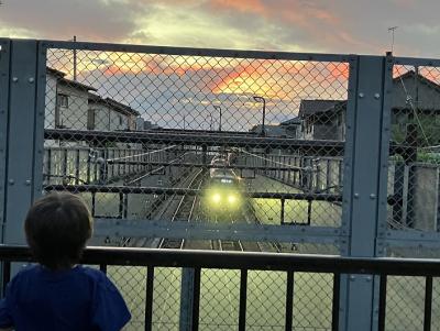 線路にかかる橋から電車と夕焼け空を見つめる子どもの写真