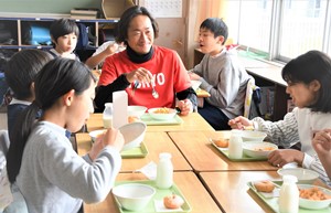 児童と一緒に給食を食べる石川クラブコミュニケーターの写真